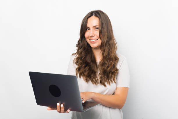 istock Playful young woman is using her laptop while standing over white background. 1341500718