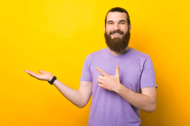Bearded man is presenting something on the yellow background. stock photo