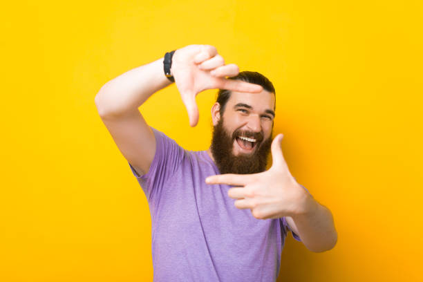 Cheerful young man is making the frame gesture over yellow background. stock photo