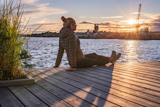Woman sits on a pier and watching the sunset stock photo