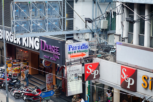 Burger King, shops and thai massage spa in Bangkok Silom seen from footbridge of BTS skytrain in Silom Road. A person is walking a person at Burger King