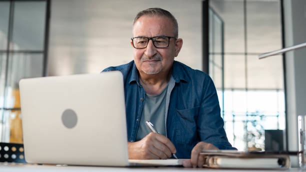 Senior man looking at laptop computer and taking notes stock photo