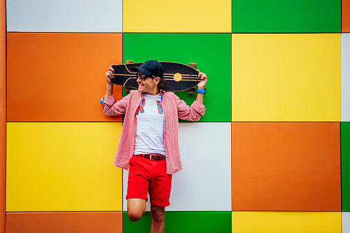 a man is leaning against a colorful wall with his head on a skateboard.