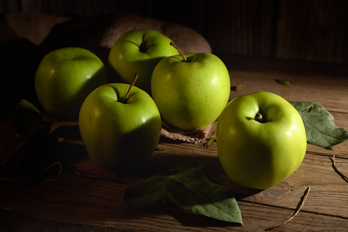 Several green apples on a sack on a rustic wooden table.