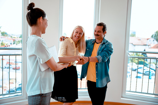 Real Estate agent shake hands with couple, congratulating for buying new flat.