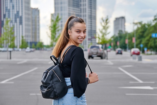 Single portrait of beautiful smiling fashionable teenage girl 14, 15 years old looking at camera, city, urban style background