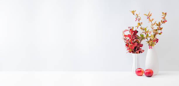 istock Home interior with decor elements. Colorful autumn leaves and red berries in a vase on a light background 1341521648