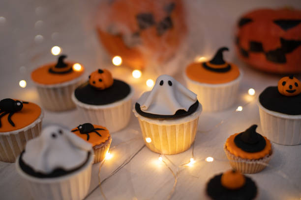 Halloween muffins with decorations in the form of ghosts, pumpkins and witch hats. A set of festive cupcakes and treats for a Halloween party. stock photo