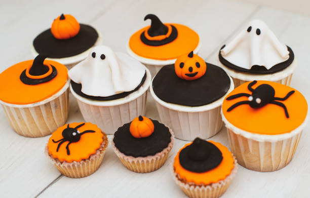 Halloween muffins with decorations in the form of ghosts, pumpkins and witch hats. A set of festive cupcakes and treats for a Halloween party. stock photo