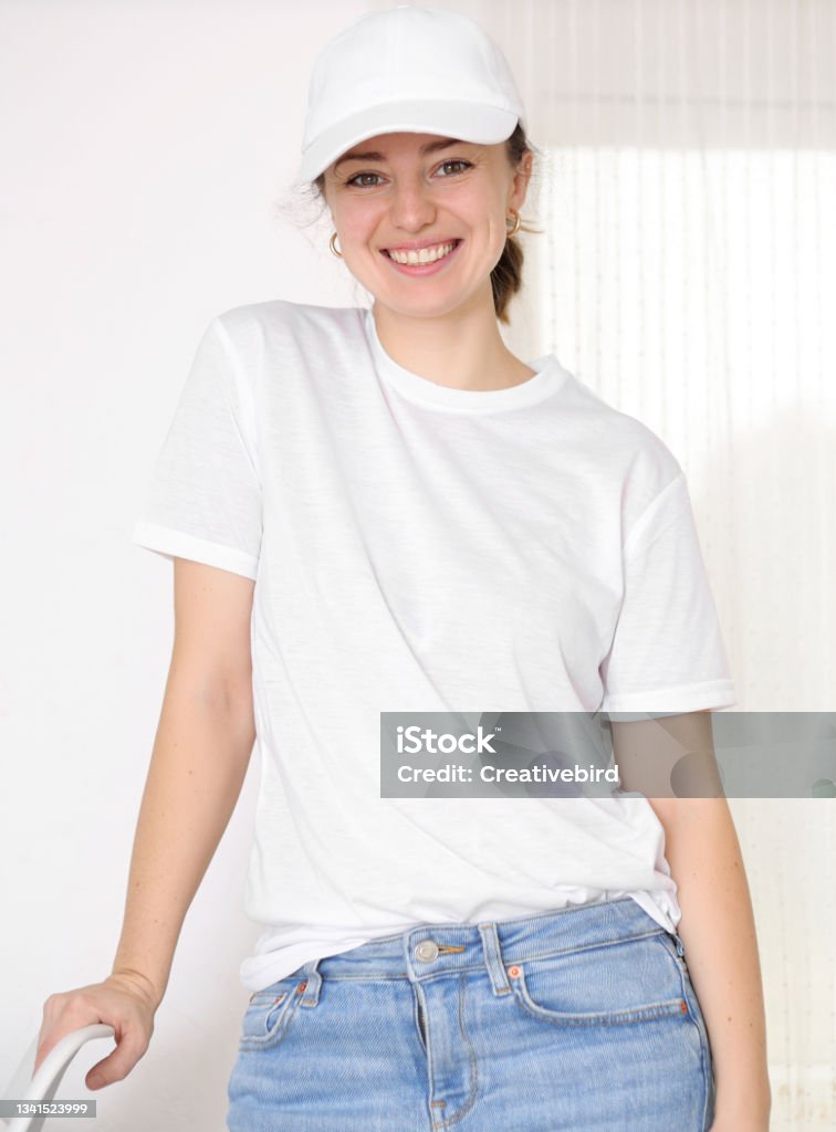 Female model wearing a white t-shirt and baseball cap. White cap and t-shirt mockup, template for picture, text or logo. Smiling attractive girl. Free space, copy space. Female model wearing a white t-shirt and baseball cap. White cap and t-shirt mockup, template for picture, text or logo. Smiling attractive girl. Free space, copy space One Woman Only Stock Photo