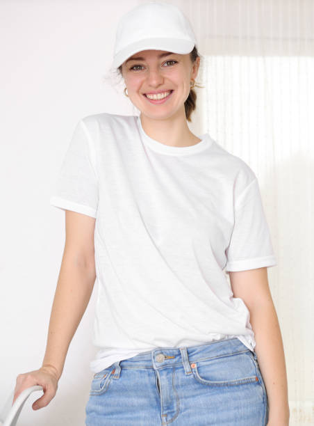 Female model wearing a white t-shirt and baseball cap. White cap and t-shirt mockup, template for picture, text or logo. Smiling attractive girl. Free space, copy space. Female model wearing a white t-shirt and baseball cap. White cap and t-shirt mockup, template for picture, text or logo. Smiling attractive girl. Free space, copy space woman wearing baseball cap stock pictures, royalty-free photos & images