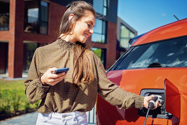 Portrait of young woman charging electric car at front of her house stock photo