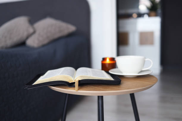 apri la bibbia con una tazza di tè e candele su un tavolo di legno in camera da letto. tempo per la preghiera. - open teaching book wood foto e immagini stock