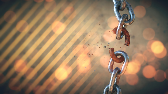 A vertical shiny chain with a rusty link in the process of breaking, isolated on a defocused industrial background with danger stripes and lens flare.
