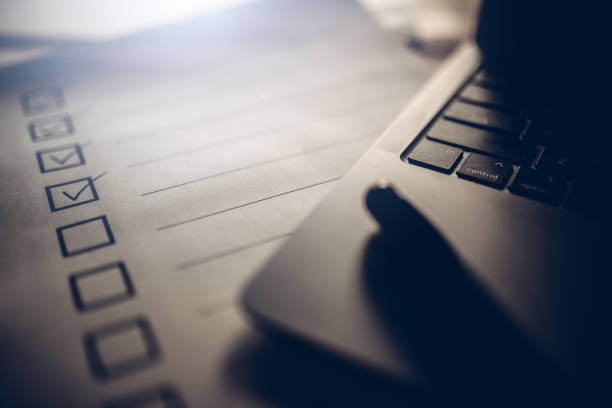 Close-up of a checklists on white paper and part of a laptop computer.