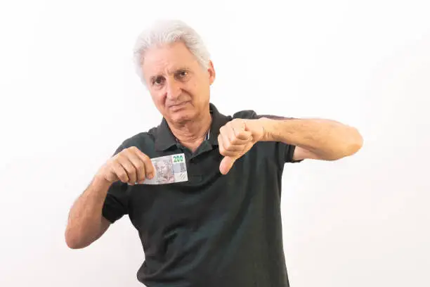 elderly man holding 200 Brazilian reais banknote with gesture in use of the great currency devaluation.