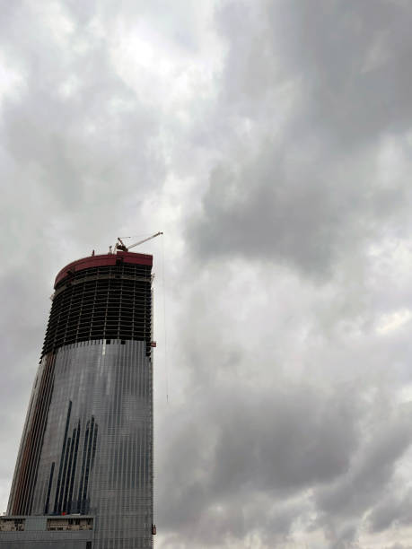 istock Modern skyscraper under construction with crane. From below of contemporary tall skyscraper with glass walls and with crane against cloudy sky in downtown 1341544092