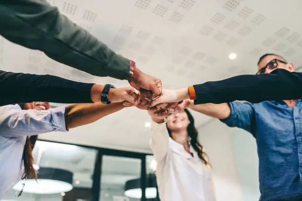 Modern businesspeople bringing their fists together while standing in a creative workplace. Diverse group of businesspeople smiling cheerfully while standing together in a huddle.