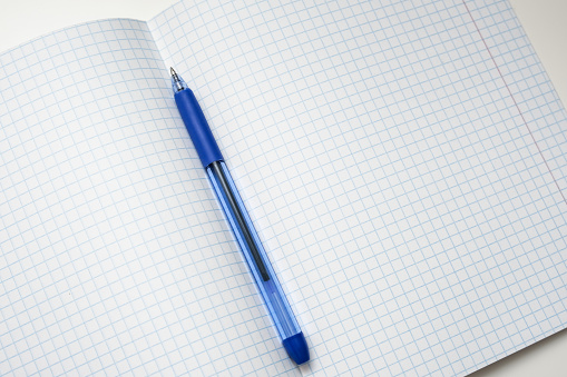 A blue ball pen lying on a blank checkered school notebook sheet , paper with copy space.