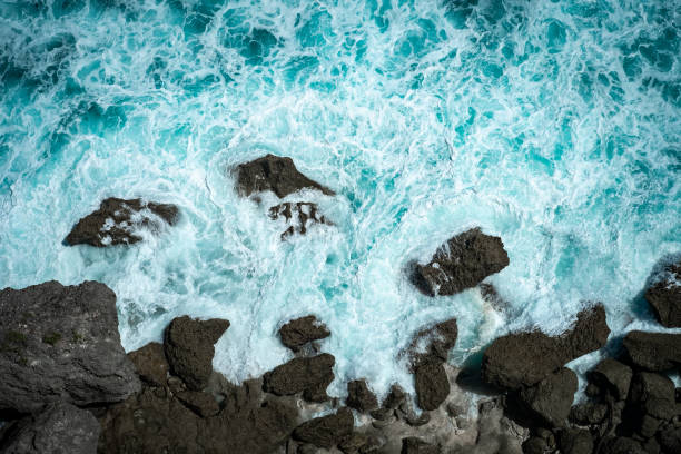 istock Raging blue ocean waves break on rocks with foam on the water, top view 1341546403
