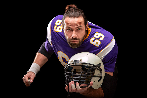 Portrait of american football player with helmet in hand close up, on black background