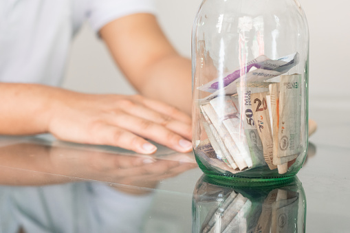 boy's hand next to his savings in a glass jar. young man next to his personal finances. bored student with a hand on his head. savings and finance concept