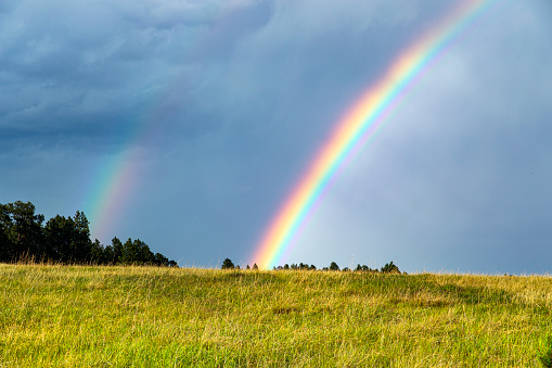 Brightly lit rainbow shining behind green grassy knoll