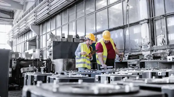 Photo of Engineers working in metal manufacturing industry, doing quality control of the production with tablet.