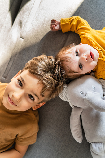 Small caucasian boy five years old lying on the bed with his baby brother or sister looking to the camera top down view
