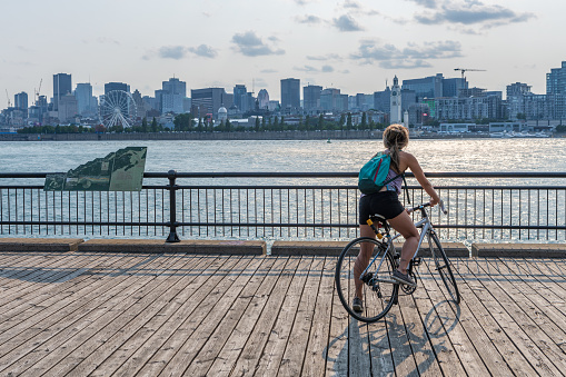 Montreal, Quebec, Canada - August 3 2021 : A woman rides a bicycle and watching the sunset in Jean-Drapeau park maritime shuttle landing stage. Saint Helens Island.