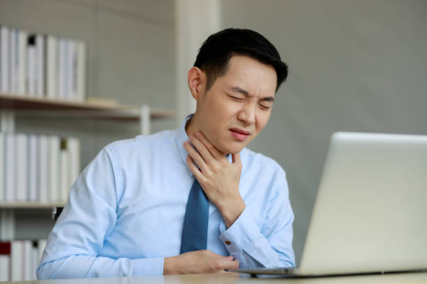 Young asian businessman sitting working with laptop at desk in the office, hand at his neck, feeling unwell, have a sore throat, Young asian businessman sitting working with laptop at desk in the office, hand at his neck, feeling unwell, have a sore throat, depression behavior businessman economic depression stock pictures, royalty-free photos & images