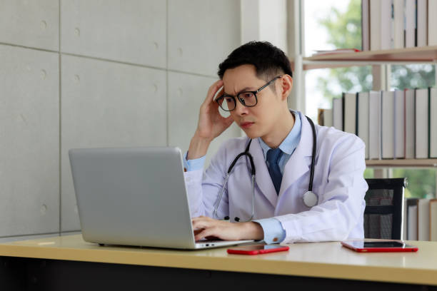 istock asian doctor sitting stressed on work space and computer on the table in his office hospital room 1341575193