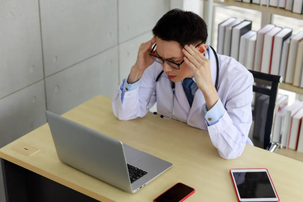 istock asian doctor sitting stressed on work space and computer on the table in his office hospital room 1341575222