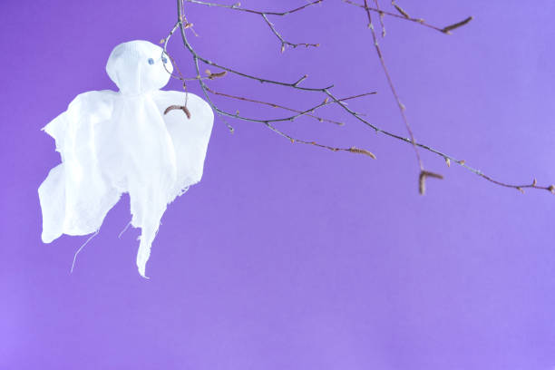 istock Halloween holiday concept. A ghost and a leafless tree branch on a purple background. 1341588893