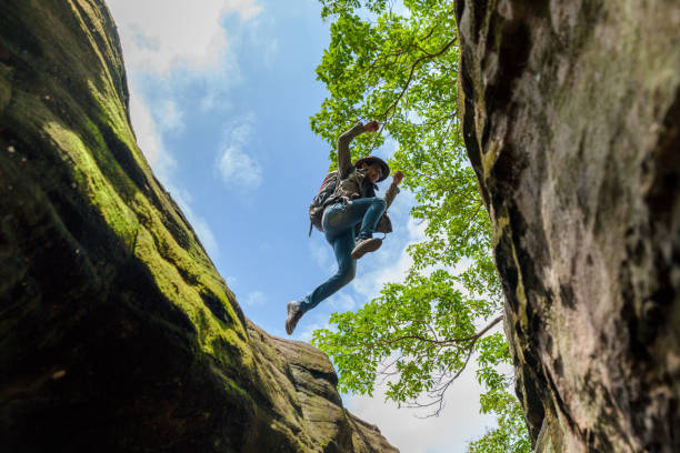 man backpacking hiking. make a jump over a steep cliff / valley. activity in holiday and hiking concept. add noise effect and film grain filter. - leadership risk cliff mountain climbing imagens e fotografias de stock