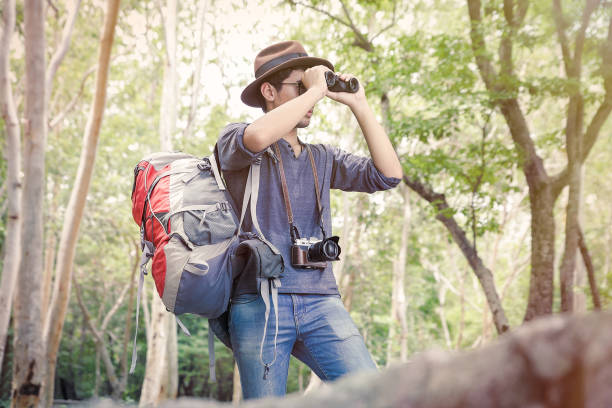 istock Man wearing a hat Have a camera And backpack He has binoculars for birds and nature in the jungle and rocks. Relaxing time camping on a mountain. Activity in holiday and hiking concept. 1341590439