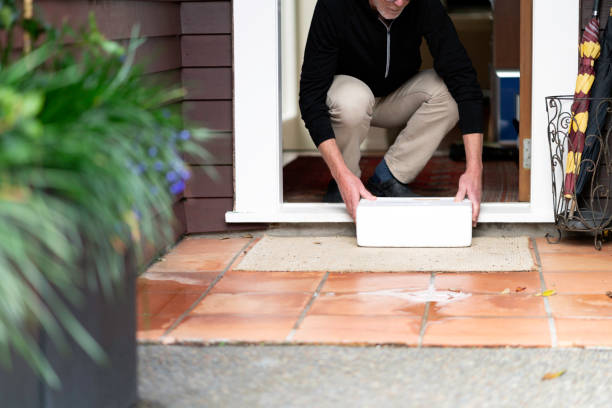 Senior male picks up a cooler bin of frozen fish at his front door Senior male picks up a polystyrene cooler box of frozen fish at his front doorstep. The box has been delivered by contactless courier during Covid-19 lockdown restrictions. doorstep stock pictures, royalty-free photos & images