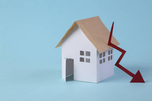 istock Falling housing prices. House figurine and falling arrow on blue background 1341595802