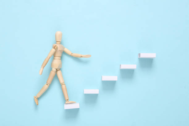 Career growth concept. Wooden puppet climbing up the steps on a blue background