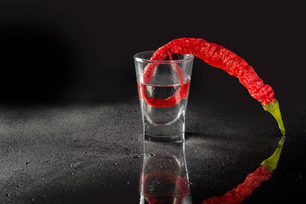 istock A stack of cold misted vodka and a pod of red hot pepper on a black background with a mirror image. Alcoholic drink, cocktail. 1341598108