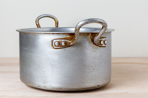 An old rough aluminum saucepan on a wooden kitchen shelf. Used dishes with scratches and marks from frequent washing