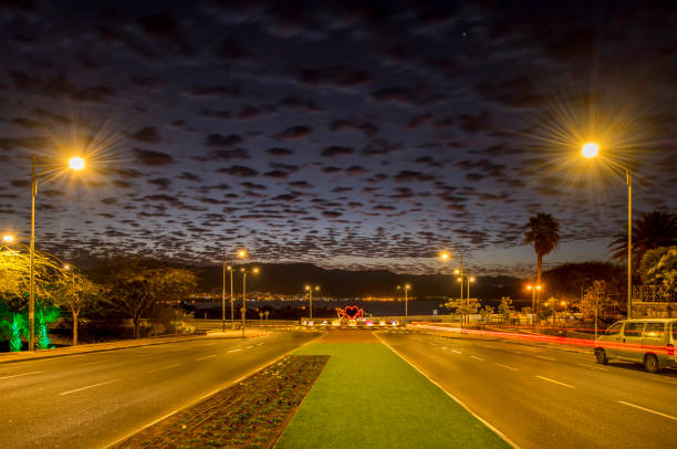 The photo depicts night street with beaming electric lamps and high clouds at the early dawn