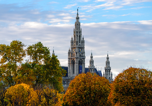 Color outdoor fall photo of the town hall of Vienna, Austria on an autumn afternoon with colorful trees and dense foliage under a blue sky with clouds