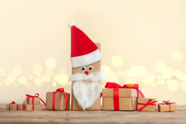 Many Handmade Christmas boxes wrapped in craft gift paper decorated with Santa Hat on wooden background with sparkling bokeh. New Year concept stock photo