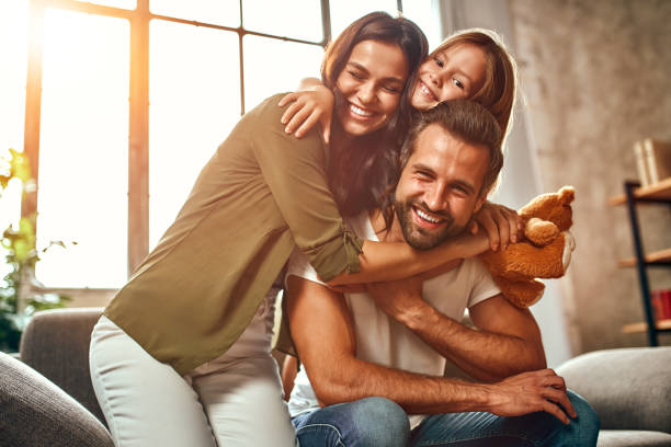 Family at home Happy dad and mom with their cute daughter and teddy bear hug and have fun sitting on the sofa in the living room at home. home lifestyle stock pictures, royalty-free photos & images