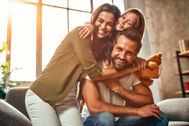 Family at home Happy dad and mom with their cute daughter and teddy bear hug and have fun sitting on the sofa in the living room at home. home interior stock pictures, royalty-free photos & images