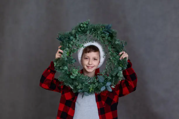 Porter of a smiling child in a red plaid shirt with a Christmas wreath. New Year and Happy Holidays