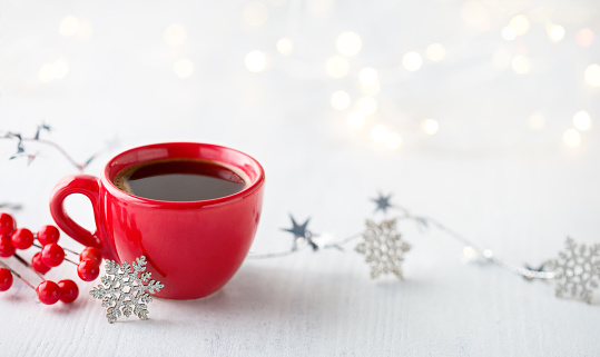 Red cup of coffee and Christmas decoration on white rustic wooden table. Shallow DOF. Selective focus.