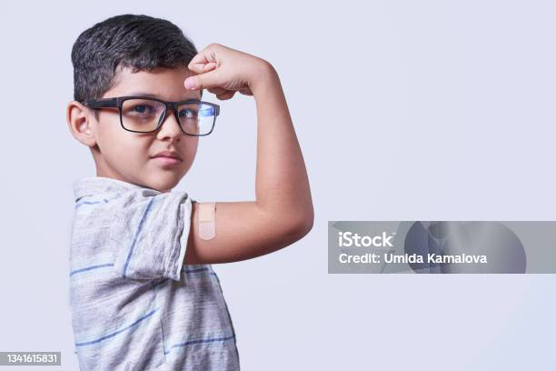 Portrait Of Happy Healthy Young Kid Showing Bandage Plaster On Arm Shoulder After Getting Vaccination Stock Photo - Download Image Now