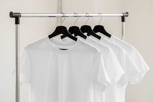 Row of white t-shirts on hangers hanging on rack